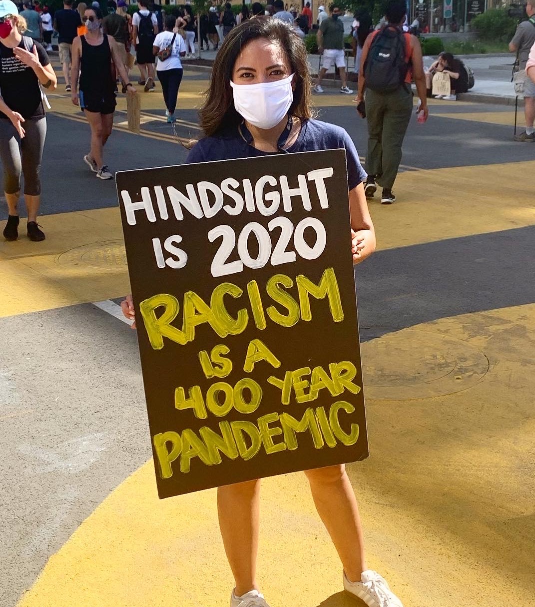 Nina Sabarre with "Hindsight is 2020. Racism is a 400 year pandemic" sign.