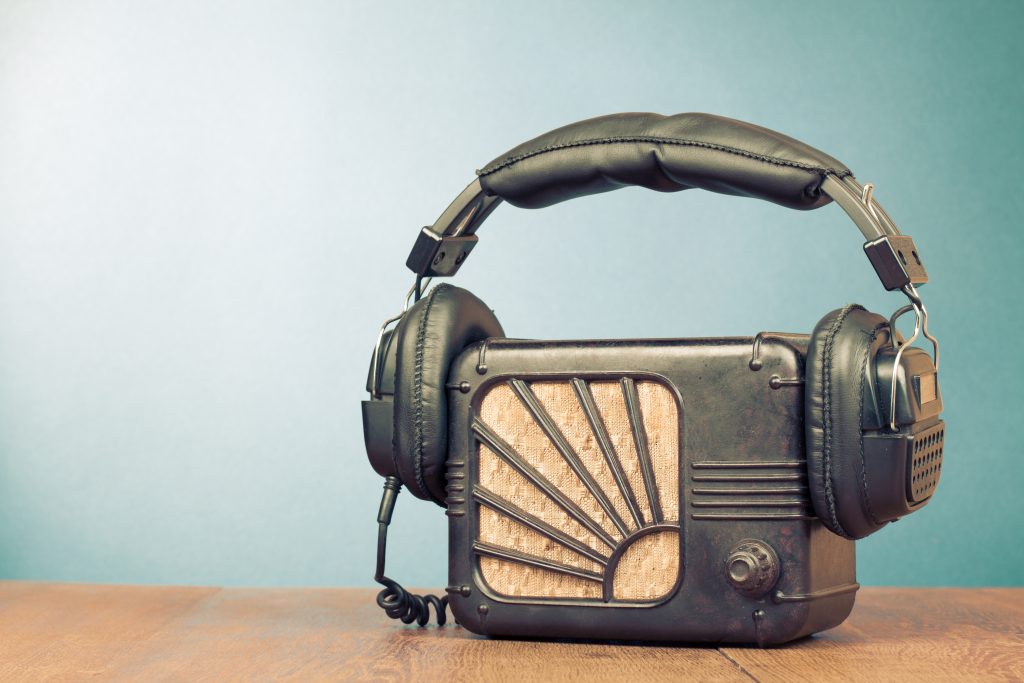 Vintage radio wearing headphones on top of a table and in front of a green wall.