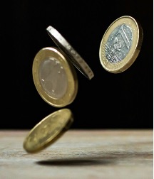 Several euro coins dropping onto a wooden table