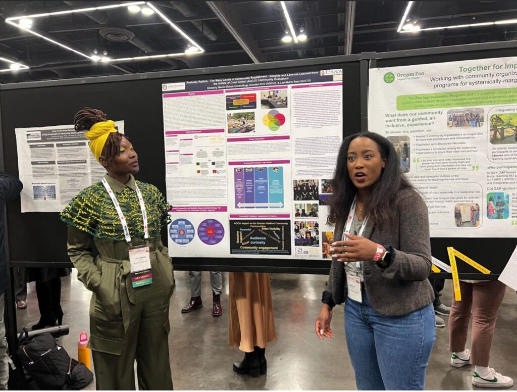 Photograph of Lael-Marie Saez and Kimolee Eryn, community evaluators partnered with Educa Consulting presenting a poster presentation at the 2024 American Evaluation Association Annual Meeting in Portland, Oregon.